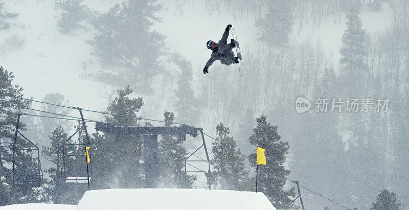 一个滑雪板在完整的冬季装备尝试一个“背部Rodeo 720鼻子抓取”的跳跃与森林和滑雪跳跃的背景在埃尔朵拉滑雪度假村附近，科罗拉多州在一个下雪的，阴天
